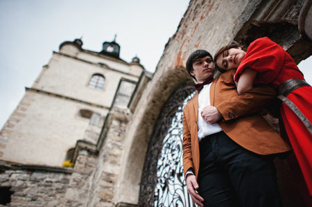 Couple hugging in love background old gates of castle. Stylish man at velvet jacket and girl in red dress in love togetherの写真素材