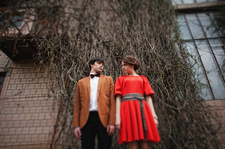 Couple hugging in love background old mansion house with large window and overgrown wall. Stylish man at velvet jacket and girl in red dress in love togetherの写真素材