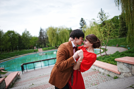 Couple hugging in love near fountain. Stylish man at velvet jacket and girl in red dress in love togetherの写真素材