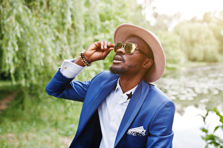 Portrait of stylish rich black man at blue jacket, hat and sunglassesの写真素材