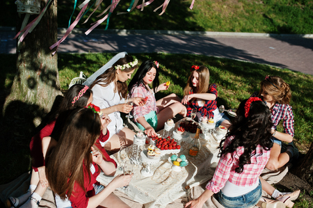 Seven happy and sexy girls sitting at picnic table and eating strawberries on bachelorette partyの写真素材