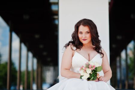 Close up portrait of big breasts brunette bride with wedding bouquet posed at wedding hallの写真素材