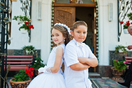First holy communion, brother and sister stay at white dress background churchの写真素材
