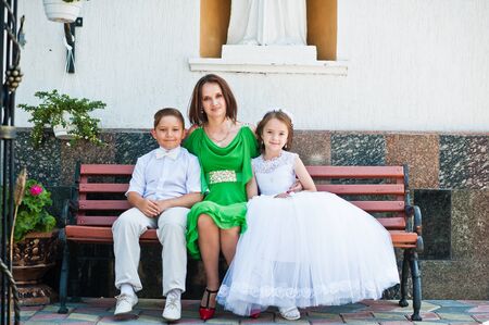 Happy family at first holy communion sitting on bench background church. Mother with sun and daughterの写真素材