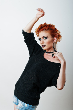 Studio portrait of red haired girl on black blouse and jeans shorts with bright dark make upの写真素材