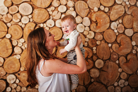 Happy caucasian mother holding on hands her baby boy background stump wooden wallの写真素材