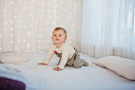 Smiled caucasian baby boy sitting on white bed with garlandの写真素材