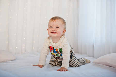 Smiled caucasian baby boy sitting on white bed with garland