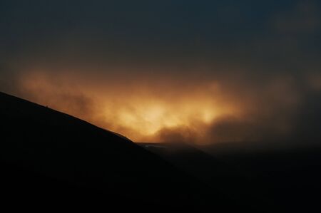 Majestic orange light of sun on dusk shadow of mountains on fog.の写真素材