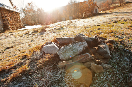 Bunch of rocks at frozen grass on mountains background house with harvested woodの写真素材