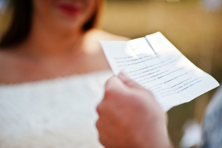 Man read vows from paper for his pregnant woman and they future baby at ceremony background white arch on gardenの写真素材