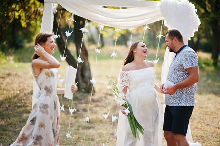 Man with pregnant woman and master of ceremony stay background white arch on gardenの写真素材