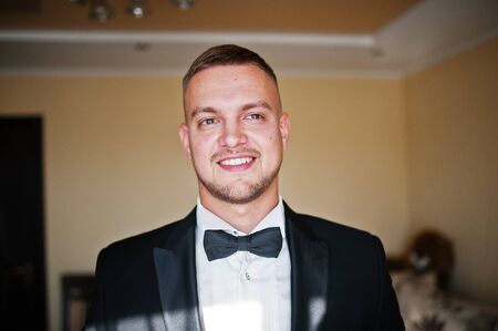 Portrait of stylish young beard man, wearing luxury jacket and bow tie. Gathering of groom on...
