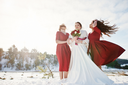 Pretty bridesmaids on red dresses with bride on sunny winter wedding day.の写真素材