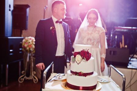 Wedding couple cut wedding cake with red roses and ribbonの写真素材