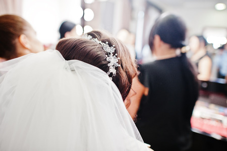 Beautiful brunette bride wearing diamond jewelery and tiara sitting on beauty salon.の写真素材