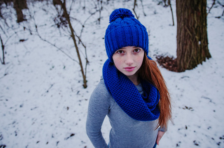 Portrait of young red hair girl with freckles wearing at blue knitted wool hat and scarf in winter day.の写真素材
