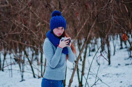 Portrait of young red hair girl with freckles wearing at blue knitted wool hat and scarf with cup of tea in winter day.の写真素材