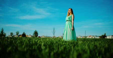 Woman in a beautiful long turqoise dress posing on a meadow on grass.の写真素材
