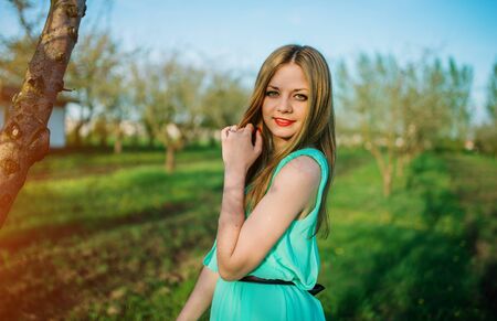 Woman in a beautiful long turqoise dress posing on a meadow in the fruit garden.の写真素材