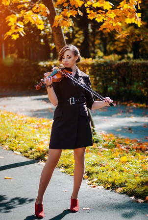 Portrait of smart girl with violin on hands outdoor in brown coat on autumn.の写真素材