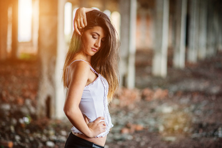Portrait of young cute brunette girl wearing on black leather pants and white blouse posed on abandoned place.の写真素材