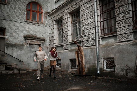 Young couple wearing on tied warm sweaters hugging in love at old yard with arch and columns at city.の写真素材