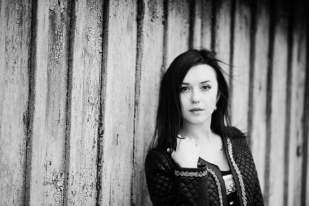 Brunette model girl at leather jacket posed background old wooden house. Black and white photo.