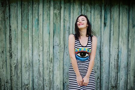 Smiling brunette model girl at dress with stripes background cian wooden background.の写真素材