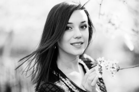 Close up portrait of young brunette girl with cherry blossom at spring garden. Black and white...