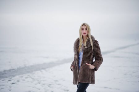 Portrait of young elegance blonde girl in a fur coat background foggy river on winter ice.の写真素材