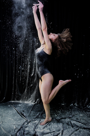 Girl dancer jumping and dancing in the white dust with flour on a black background. Studio shot of woman dancing with flour.の写真素材
