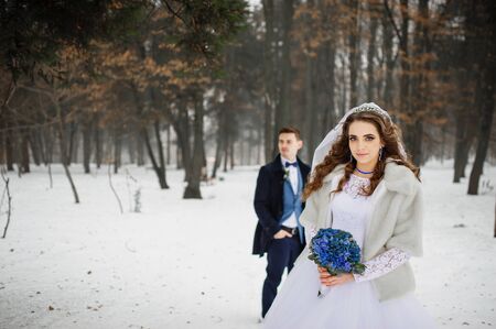 Young stylish wedding couple at forest on winter day. Loving newlyweds on snowy weather. Bride on focus background groom.の写真素材