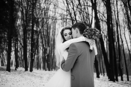 Young stylish wedding couple at forest on winter day. Loving newlyweds on snowy weather. Black and white photo.の写真素材