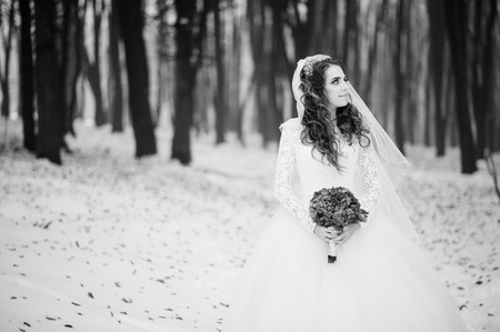 Pretty young bride with blue wedding bouquet at winter day on wood. Black and white photo.の写真素材