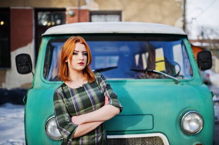 Young red haired girl posed on checkered dress background old retro cyan minivan.の写真素材