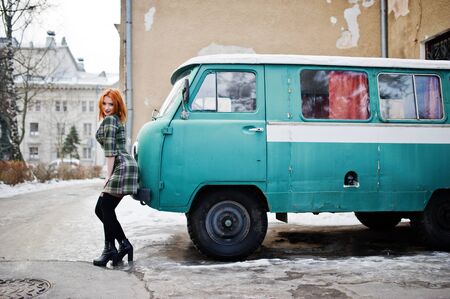 Young red haired girl posed on checkered dress background old retro cyan minivan.の写真素材