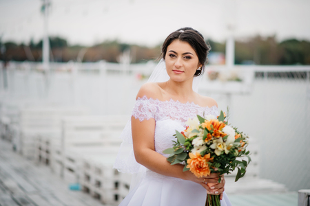 Brunette bride stay on the pier berth at cloudy day.の写真素材