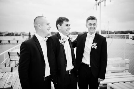 Groom with best mans posed on the pier berth at cloudy wedding day. Black and white photo.の写真素材
