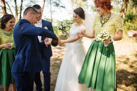 Wedding couple with bridesmaids and best drinking champagne at sunny wood.の写真素材