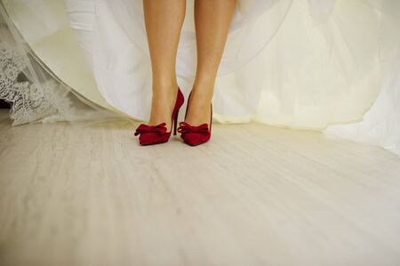 Red velvet shoes on legs of bride.の写真素材