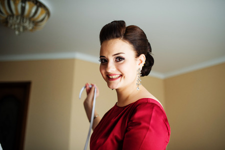 Cheerful brunette bridesmaid on red dress tie bow on wedding dress of bride.の写真素材