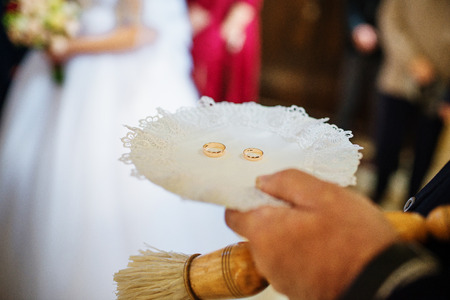 Wedding rings on plate at hand of priest at wedding ceremony at church.の写真素材