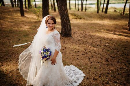 Amazing brunette bride with violet wedding bouquet at pine wood.の写真素材