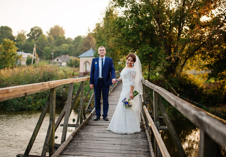 Cheerful wedding couple on wooden bridge at sunset.の写真素材