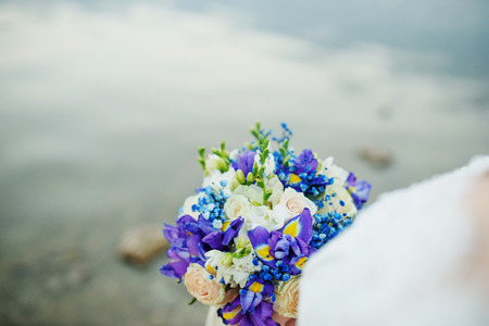 Amazing violet and white wedding bouquet at hands of bridde against water of river.の写真素材