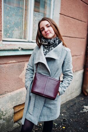Young model girl in a gray coat with leather handbag on shoulders posed background vintage house.の写真素材