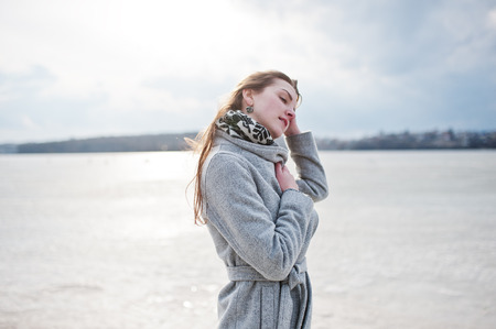 Young model girl in gray coat with red hair against freeze lake.の写真素材