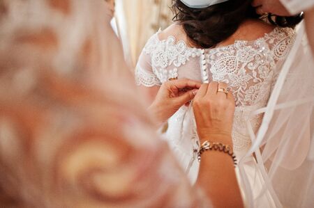 Bridesmaids helped dressed wedding dress for bride at room.の写真素材