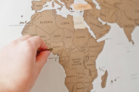 Scratch travel map of the world. Hand of man erase Africa Nigeria with coin.